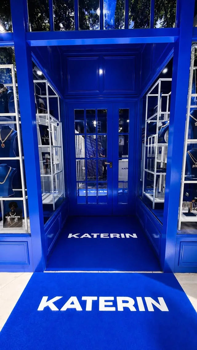 Entrada de la tienda KATERIN en Barcelona: fachada, puerta y alfombra en azul Katerin con el logotipo en blanco.